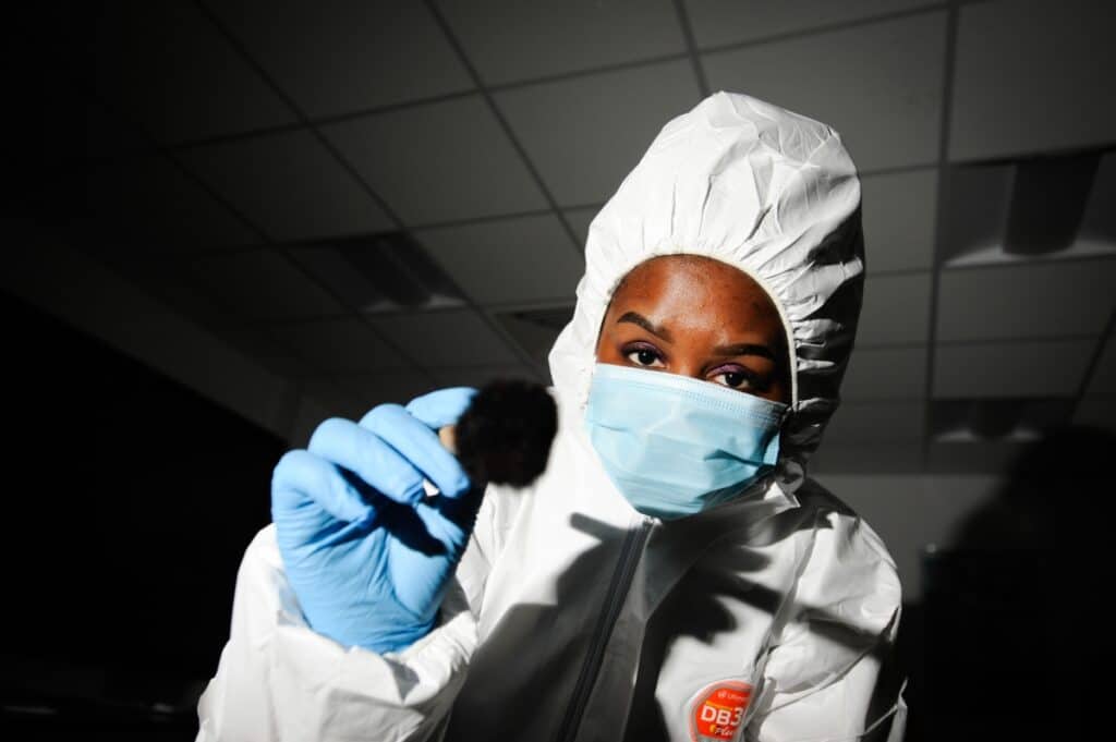 A forensic science student in a mask and body suit dusts for fingerprints