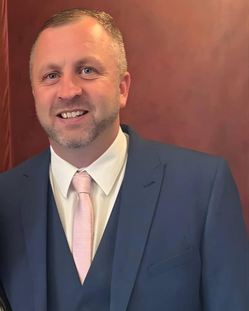Male in a blue suit smiling against a brown background