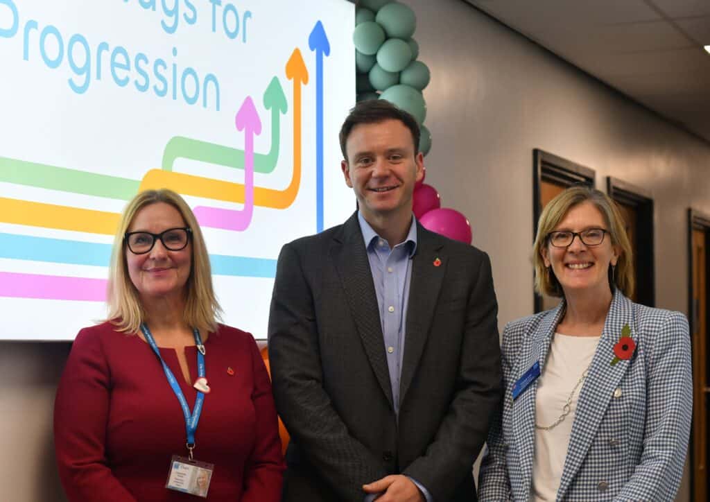 Jackie Grubb , Fred Thomas and Tracey Lee pose and smile next to the multi-coloured Pathways for Progression logo