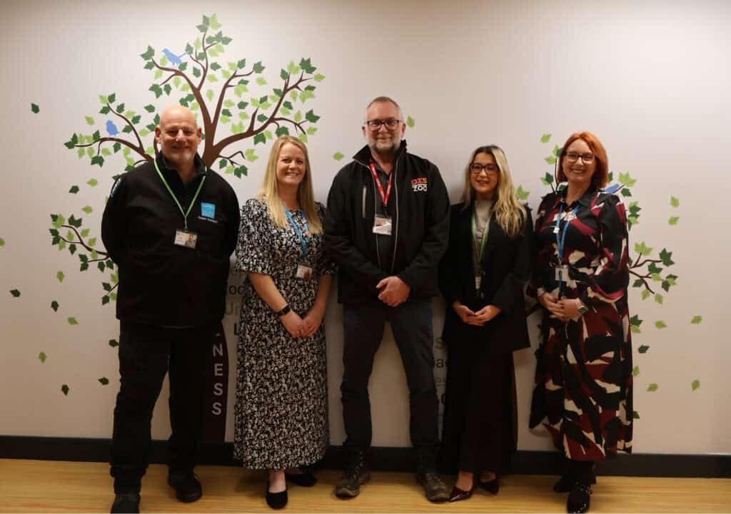 City College staff pose with Dartmoor Zoo CEO Dave Gibson in front of a wall painted with trees