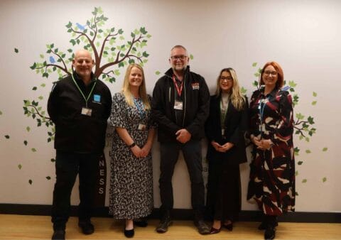 City College staff pose with Dartmoor Zoo CEO Dave Gibson in front of a wall painted with trees