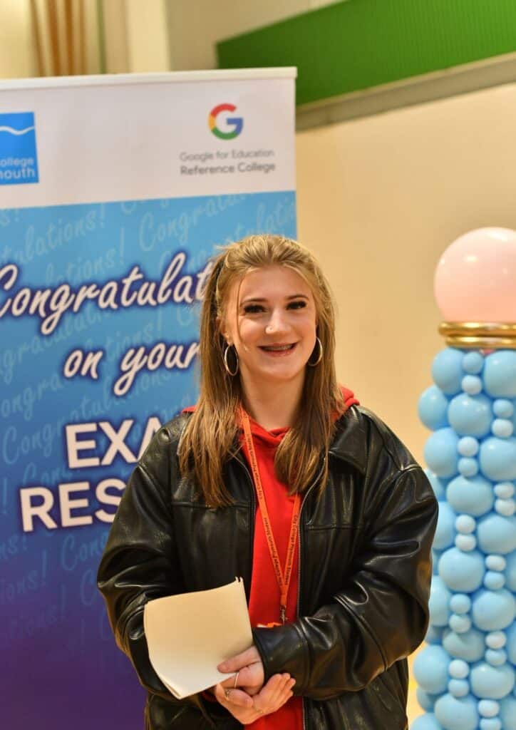 Female student in red and black poses with her gcse result envelope in the City College Sports Hall