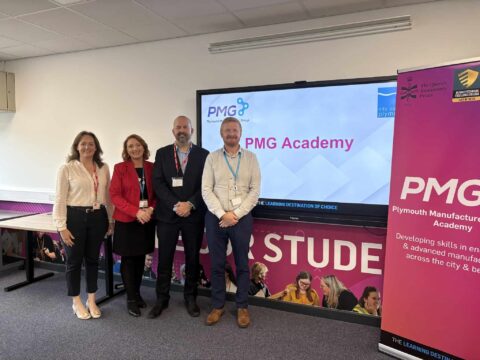 Four members of staff pose by the PMG academy sign at City College Plymouth