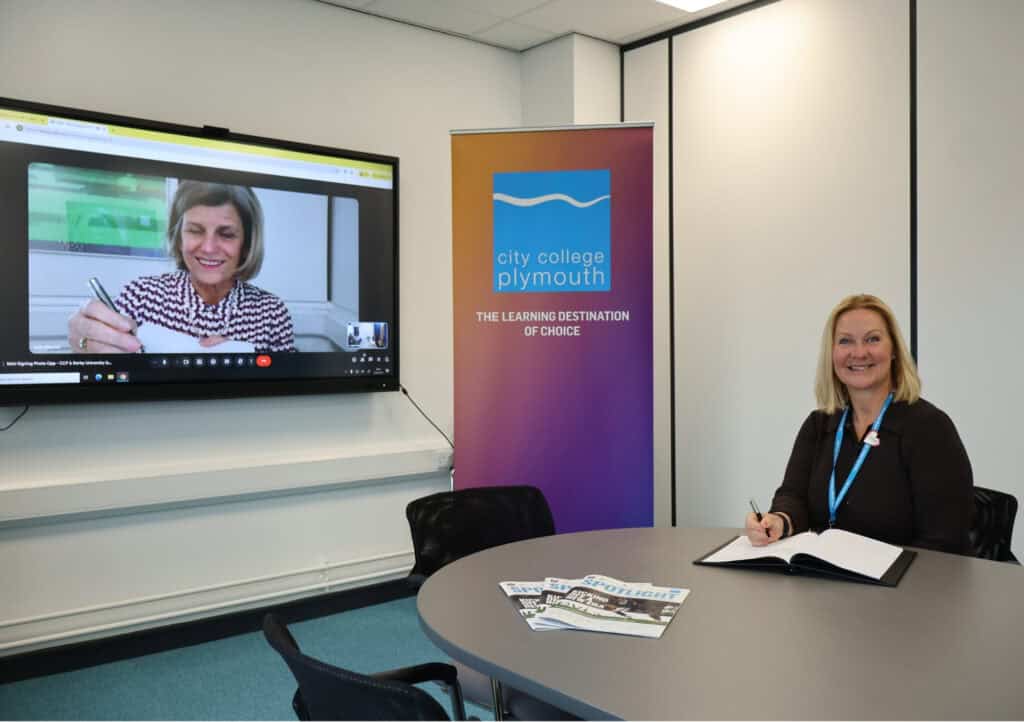 CEO of City College Plymouth Jackie Grubb sits at her desk with the MoU and a pen as her Australian counterpart looks on from a big screen, also holding a pen